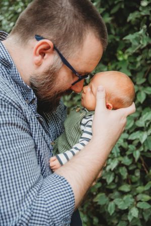 Tender moment between parent and baby against green foliage background.