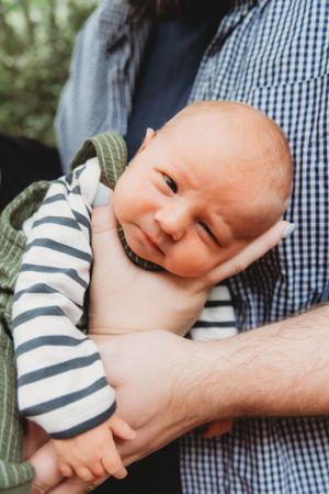 Smiling baby in striped sleeves and green wrap being held securely.
