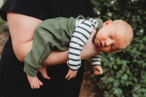 Baby in striped onesie and green wrap being held against dark background.