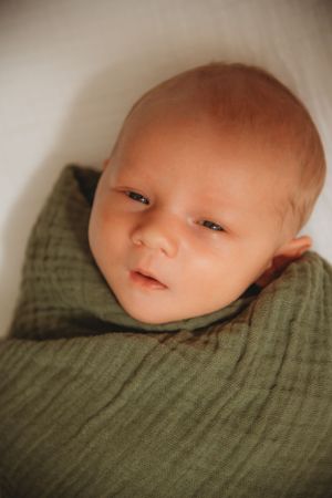 Close up of infant in green swaddle looking at camera.