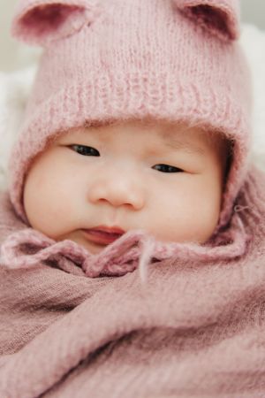 Baby wearing a pink knit hat and scarf in a cozy close-up portrait.