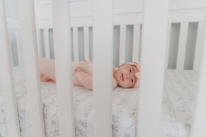 Baby peeks through white crib slats with floral bedding visible.