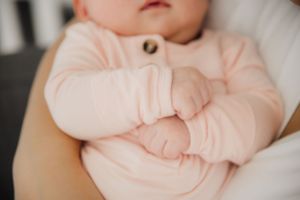Baby wearing soft pink clothing rests on white bedding.