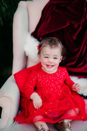 Joyful young child wearing red sparkly dress smiles brightly in holiday portrait setting.