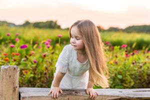 Golden hour light illuminates a garden scene with figure leaning on wooden fence.