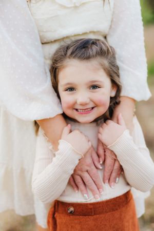 Portrait of child in cream sweater and orange pants with joyful expression.