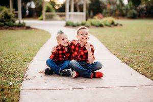 Two kids wearing matching red plaid shirts laughing together on garden path.