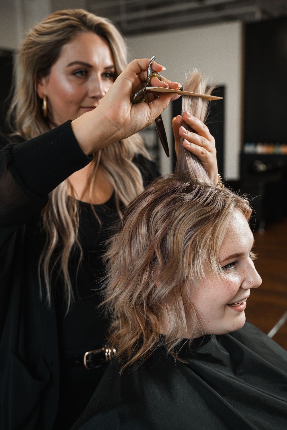 Professional stylist trimming client's hair at upscale salon.