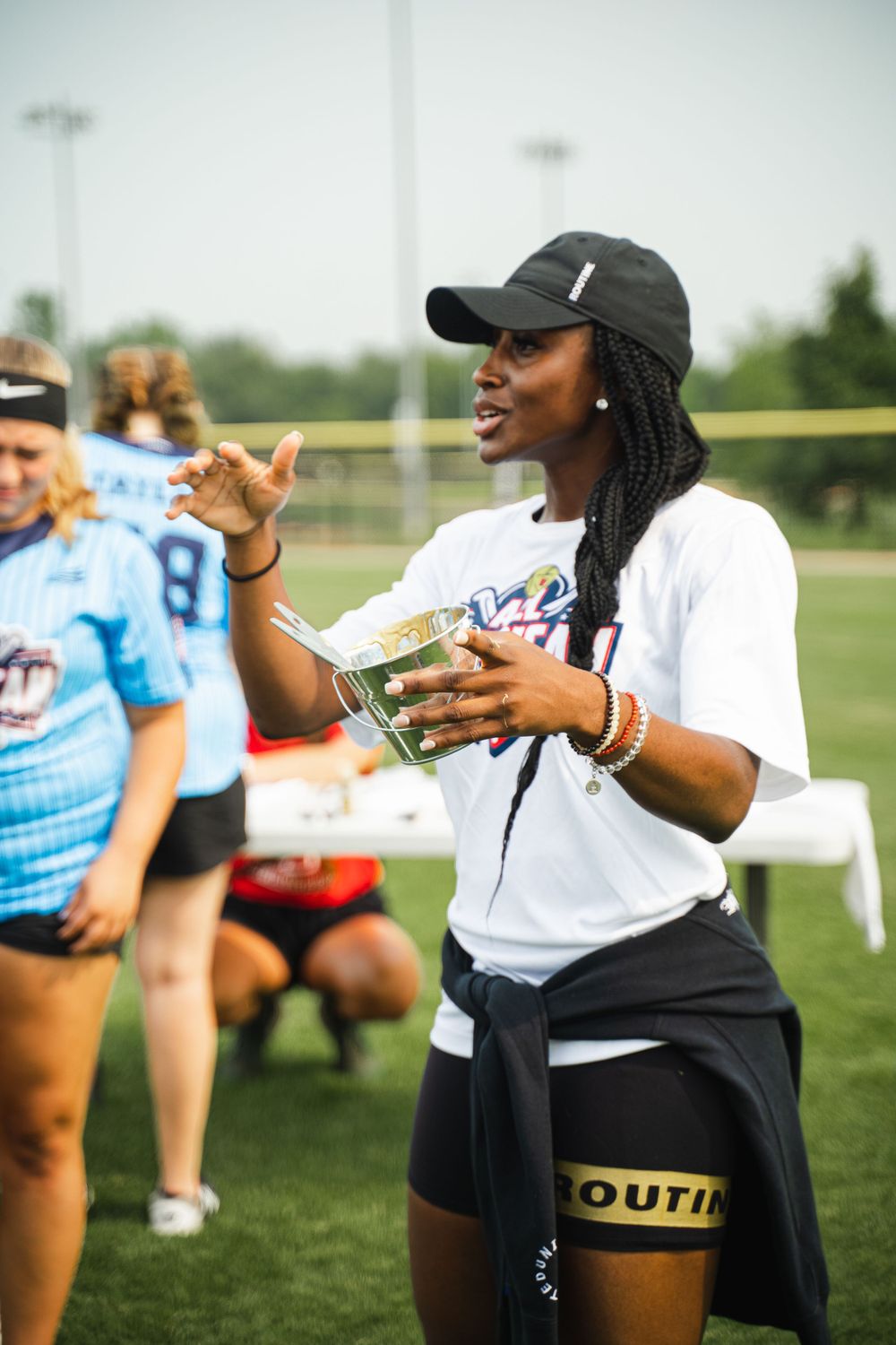 Athletic coach gestures while holding notes during an outdoor sports event on a grass field.