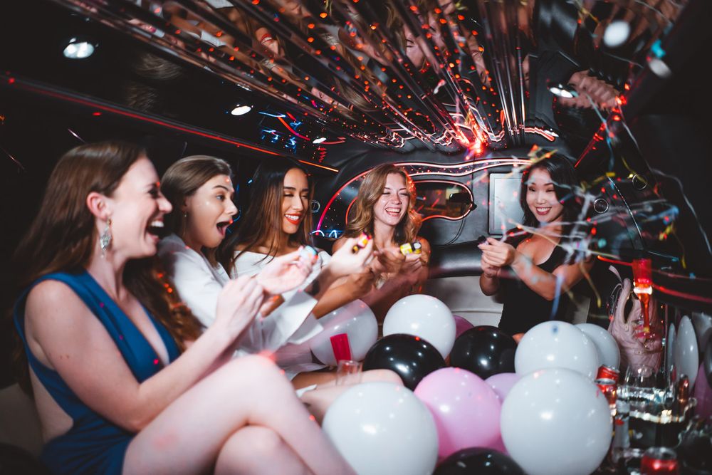 Group celebrates in limousine surrounded by white and pink balloons.