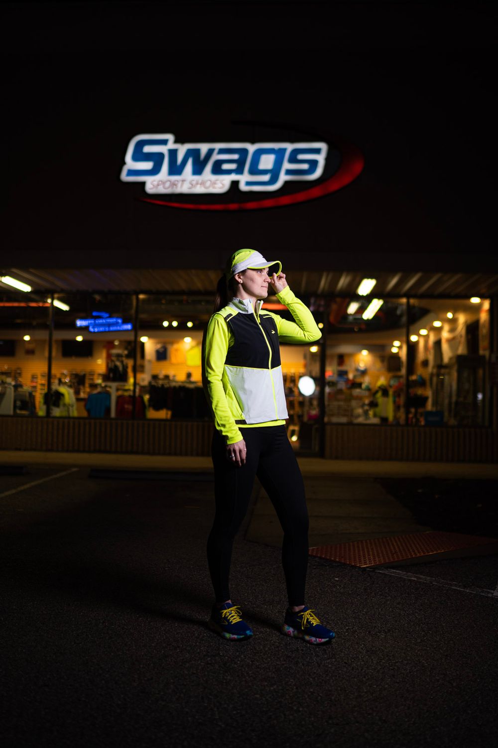 Person in high visibility safety gear and black clothing stands under illuminated sign at night.