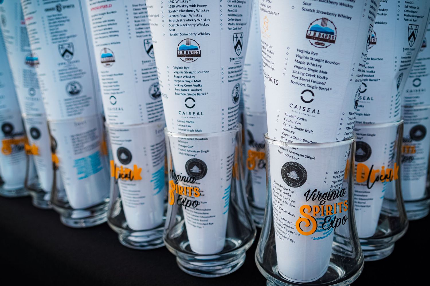 Row of branded glass drink vessels with printed menu text lined up on black surface.