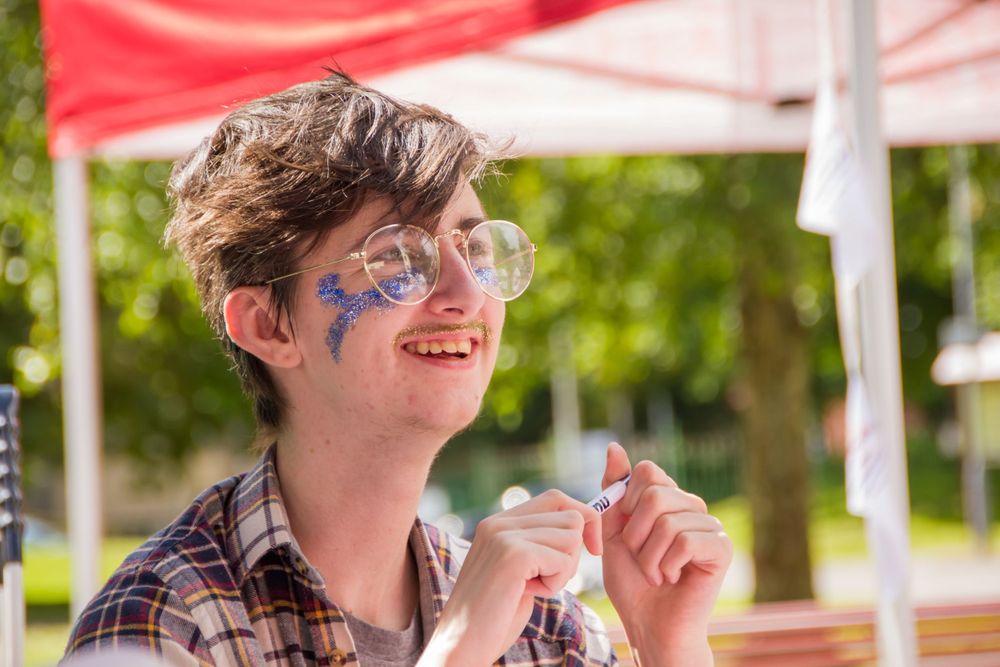 A person wearing glittery face paint and sunglasses at an outdoor festival.