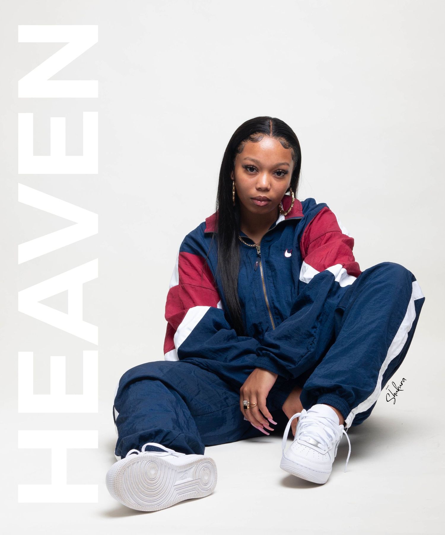 Model in blue and red tracksuit sits casually against white background with Heaven text.