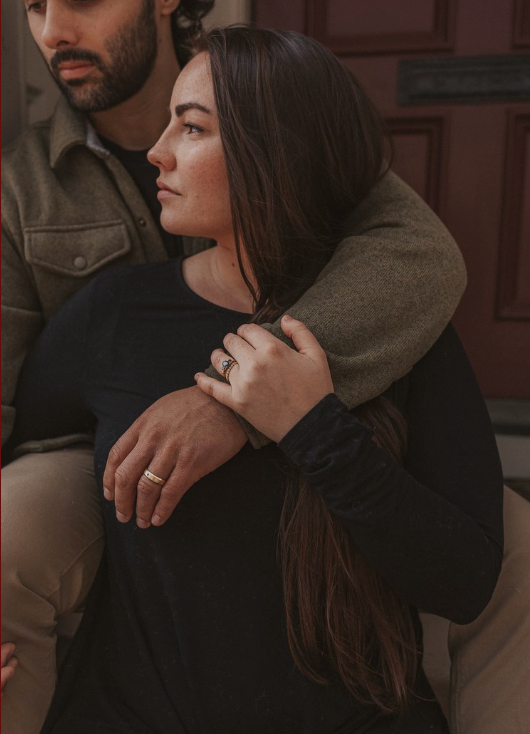 A couple embraces intimately in a dimly lit setting with moody brown tones and romantic atmosphere.