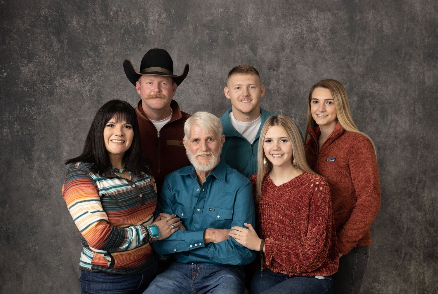 Multi-generational family portrait in western wear against textured gray background.