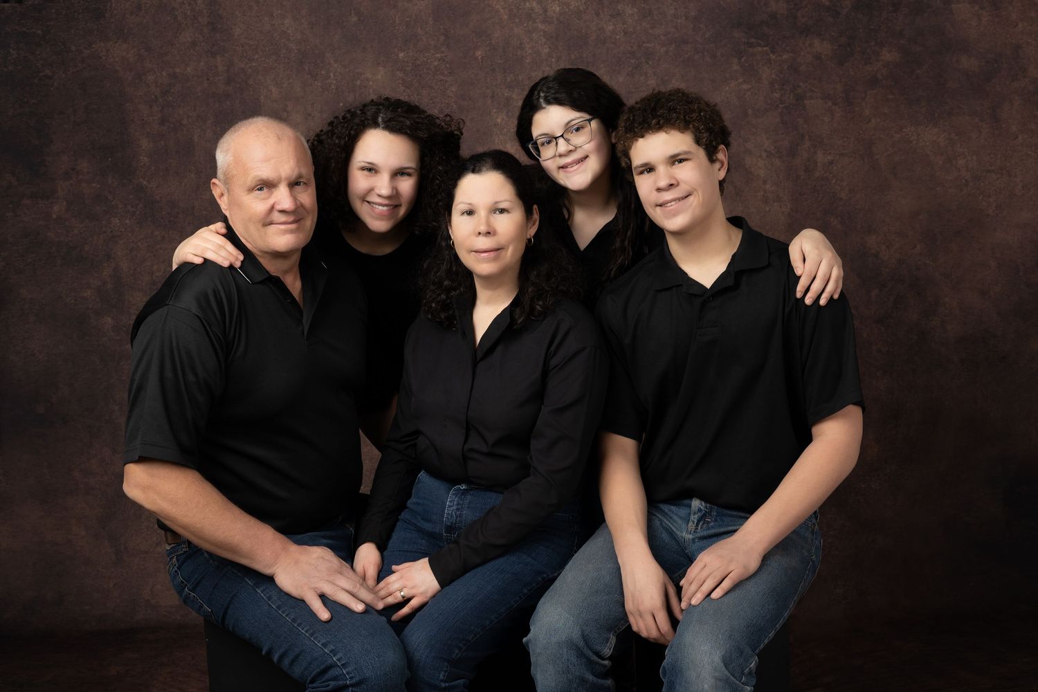 Studio portrait of family group wearing black outfits against brown background.
