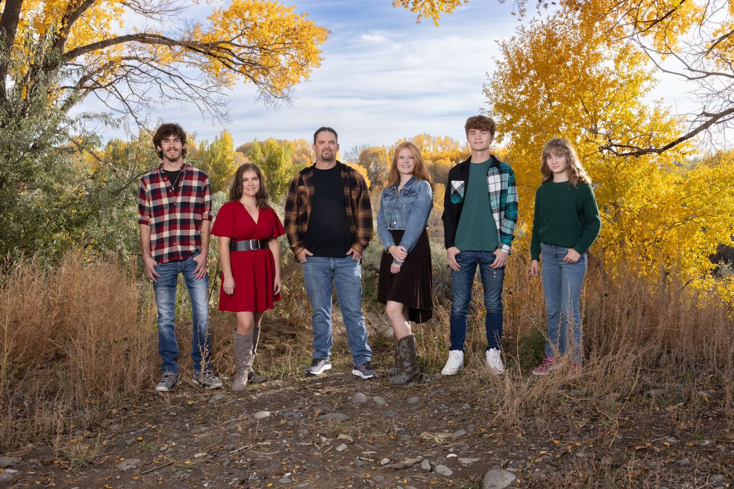 Group standing together on dirt path with vibrant autumn foliage and yellow trees in background during sunset.