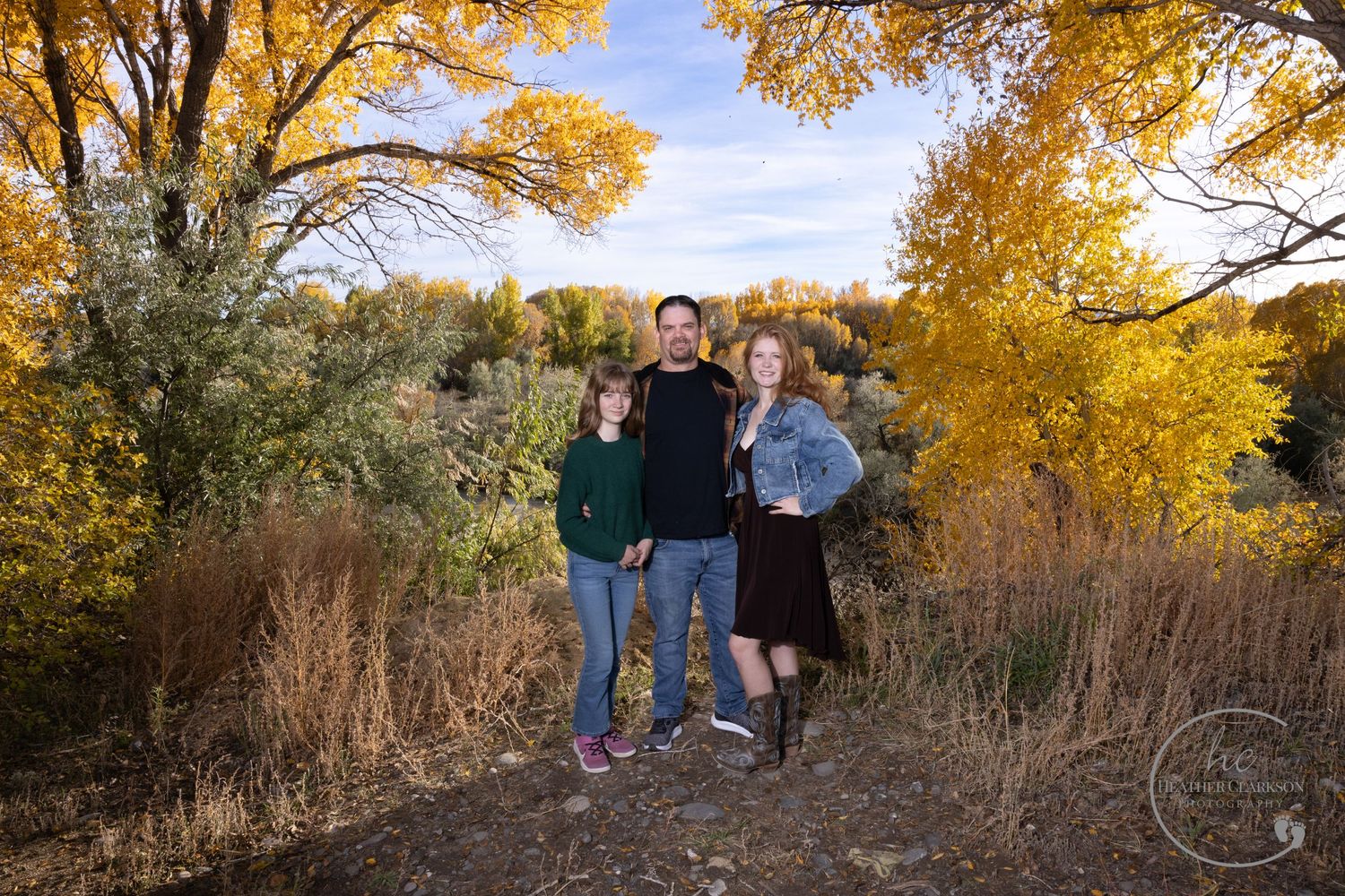 Couple posing on trail with golden fall foliage and blue sky in background.
