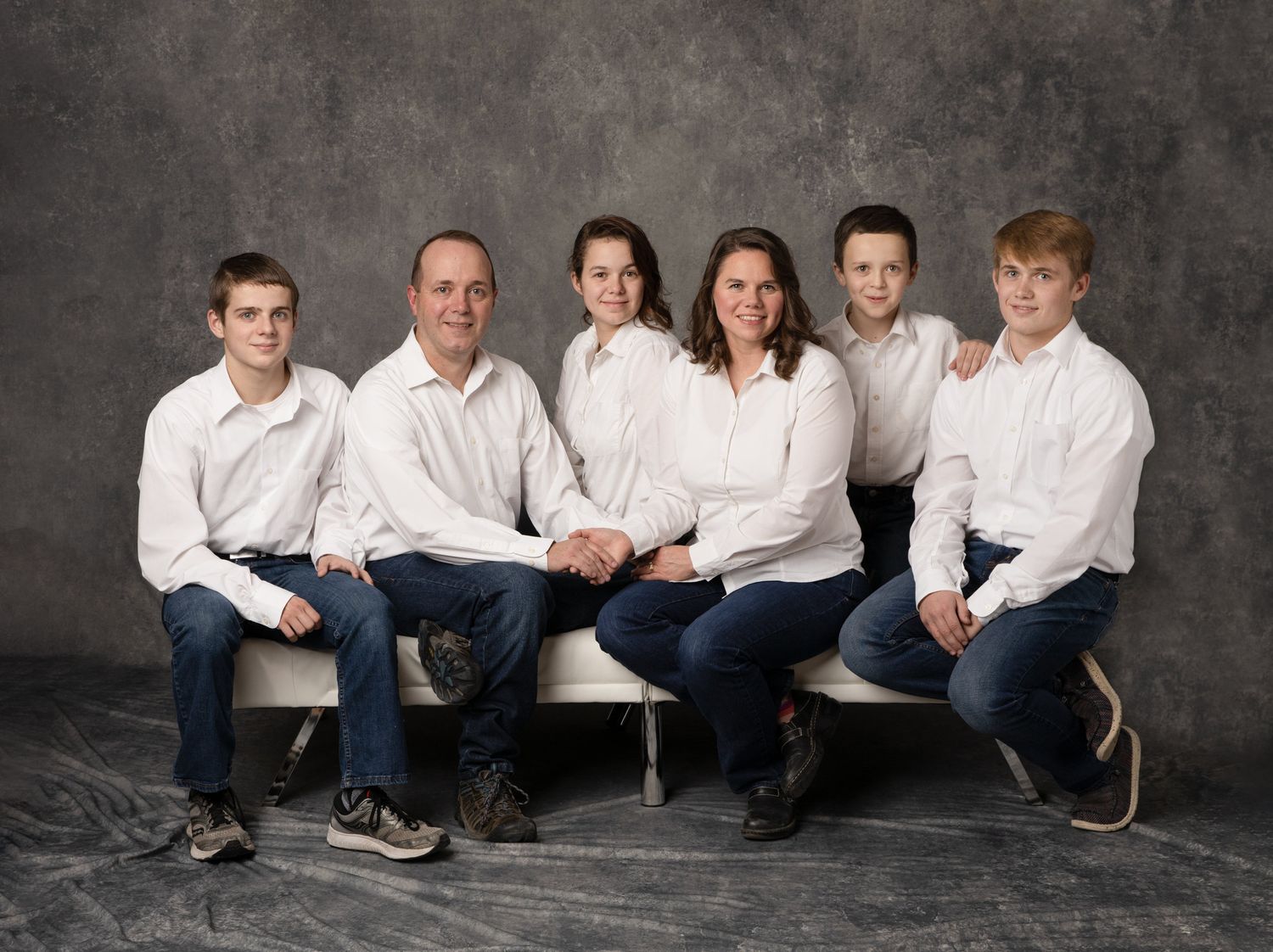 Family members wearing coordinating white shirts sit together against a dark backdrop in a professional studio portrait.