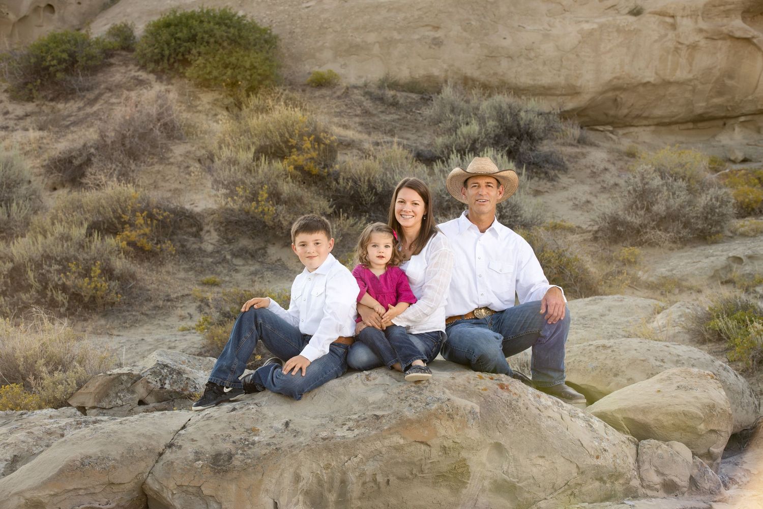 Family group poses casually together on rocky desert terrain during outdoor photo session.