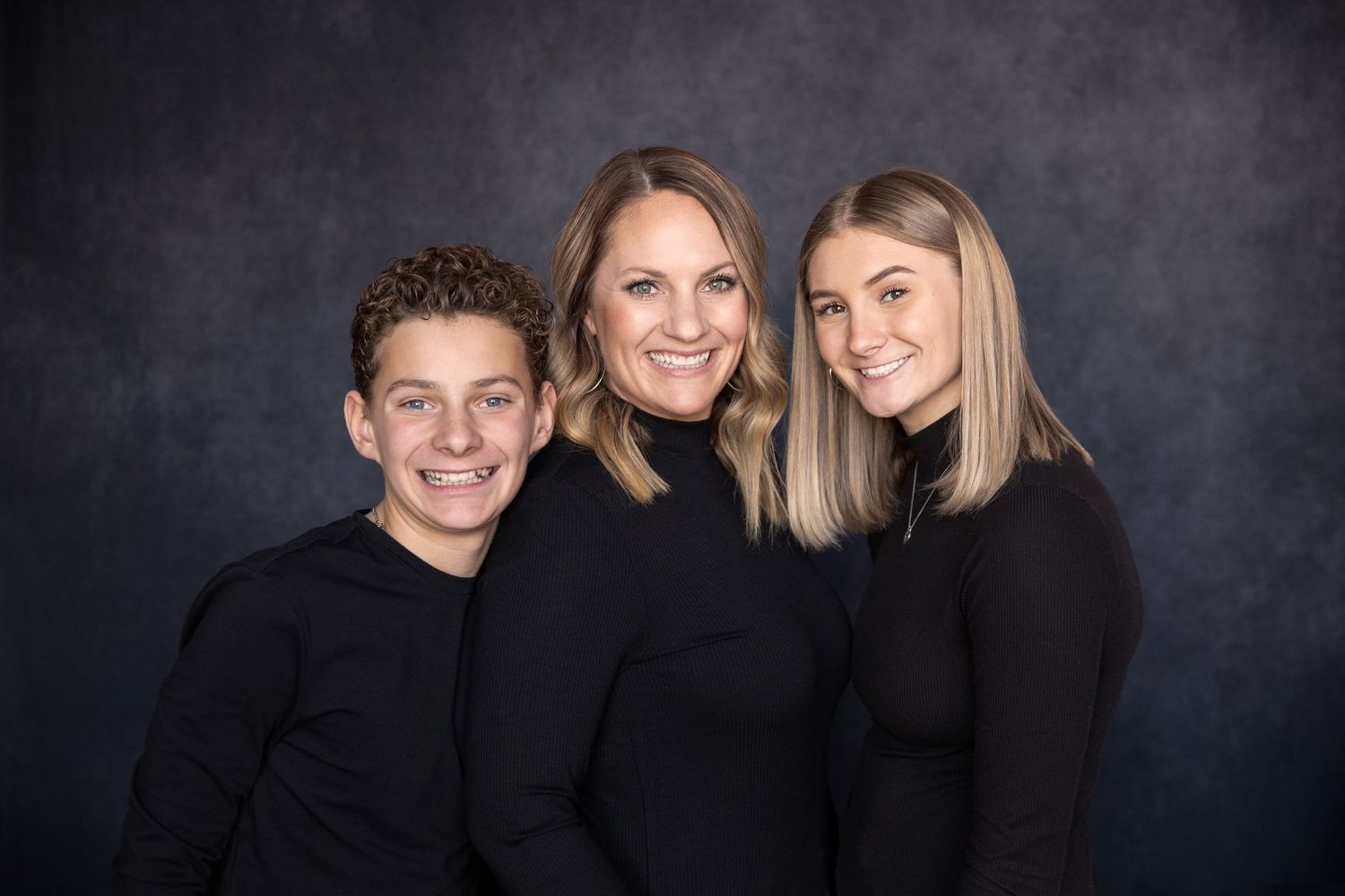 Studio portrait of family members wearing dark clothing against a moody black background.