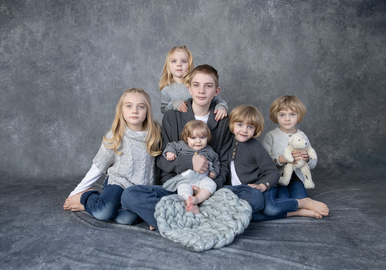 Family members lie casually together on grey floor during relaxed studio photo session.