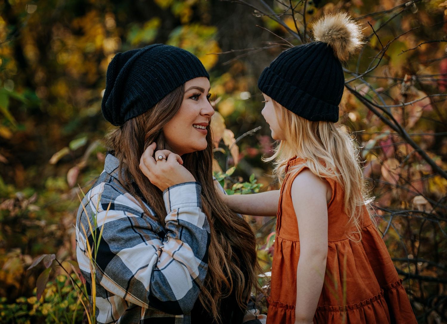 Two people in winter hats sharing an intimate moment among autumn foliage.