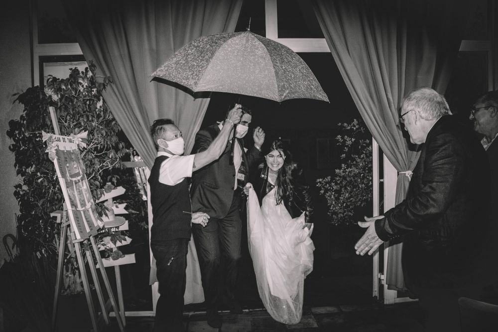 Black and white photo of wedding party celebration with umbrellas indoors.