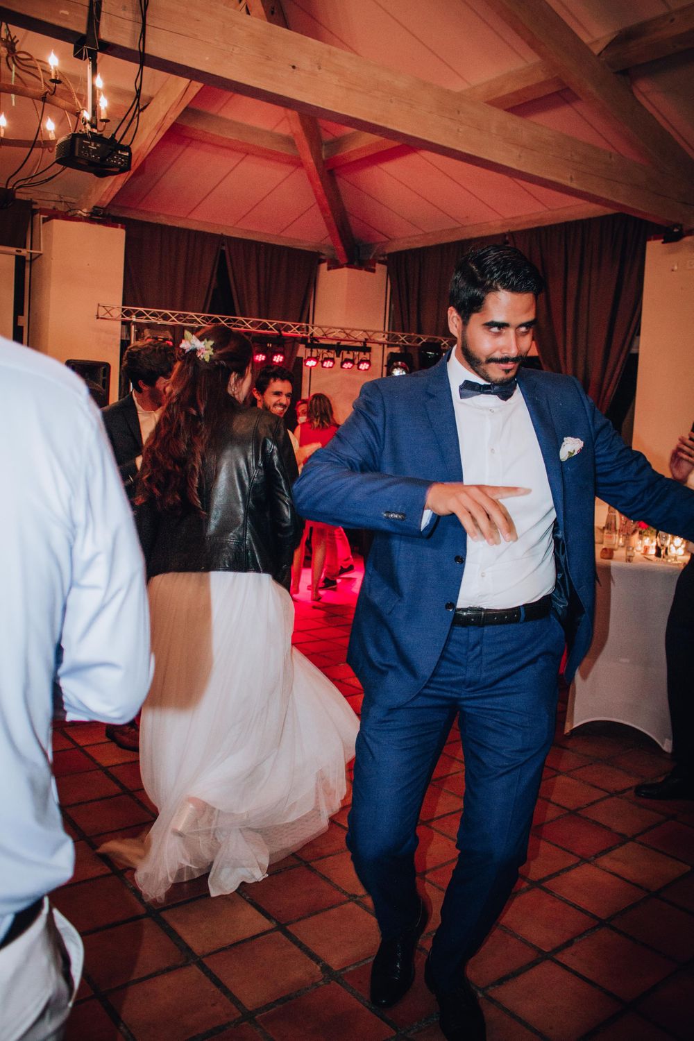 Guest in blue suit and bowtie dancing at an indoor wedding reception.