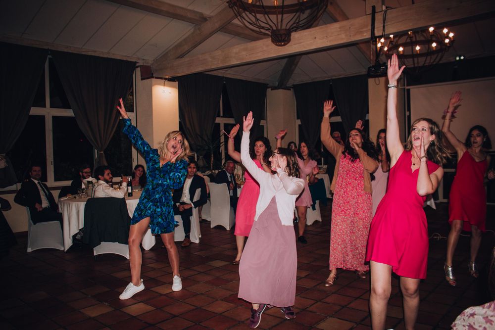 Wedding guests dancing and celebrating in colorful dresses at indoor reception.