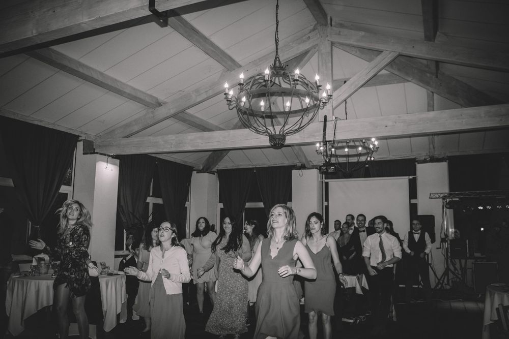 Black and white photo of wedding guests dancing under chandelier at reception.
