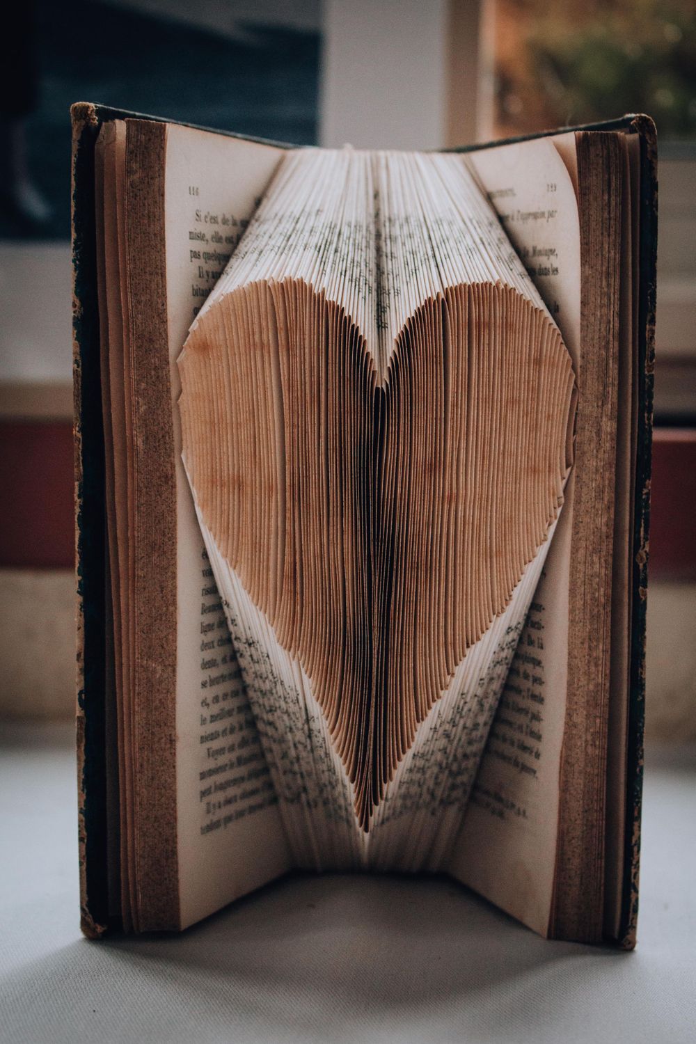 Old book with pages folded into a heart shape creating dimensional paper art.