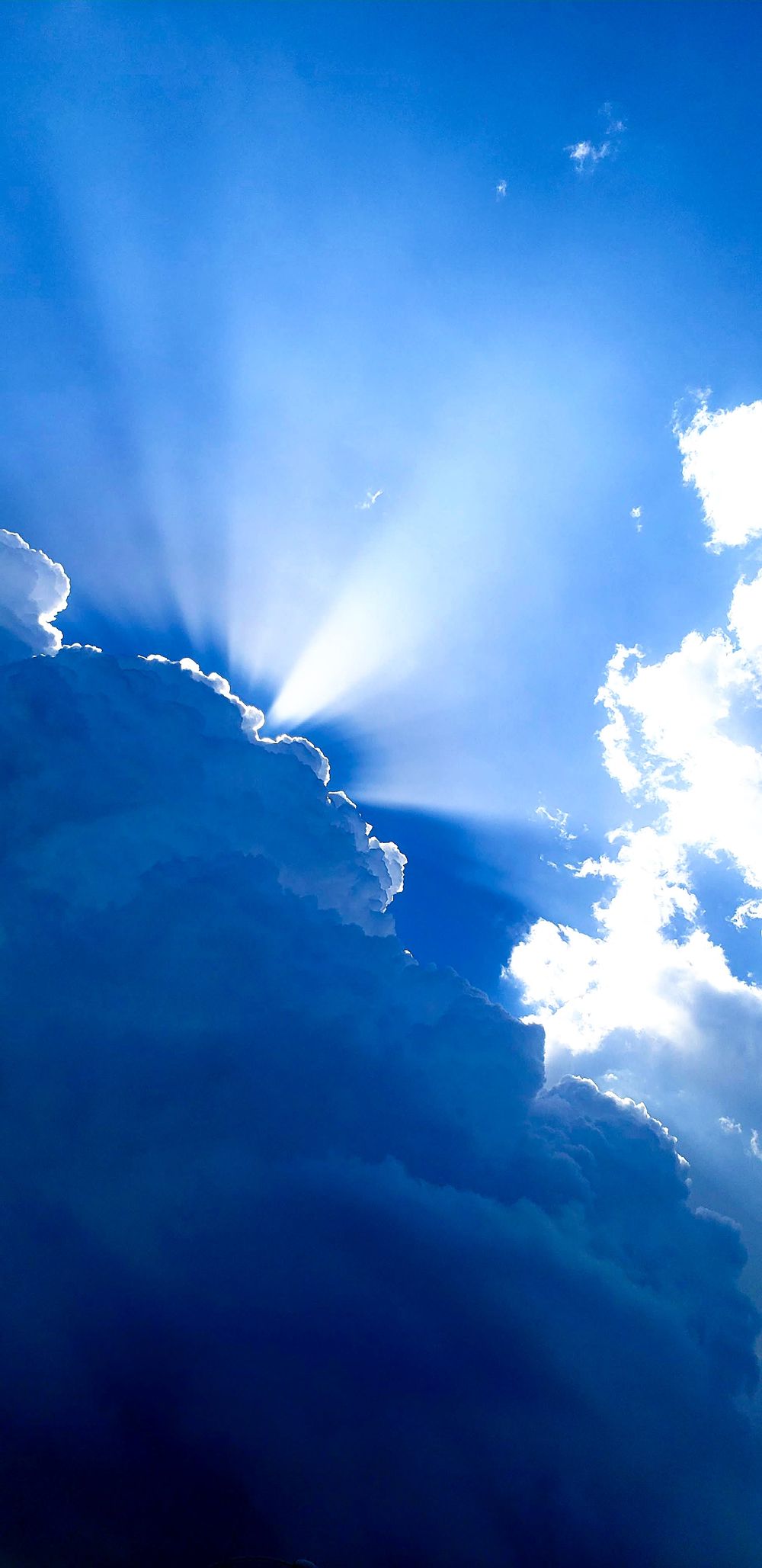 Dramatic sunbeams breaking through clouds in a bright blue sky.