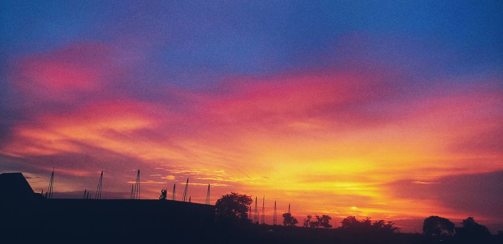 Vibrant sunset sky with silhouettes of buildings and wind turbines.