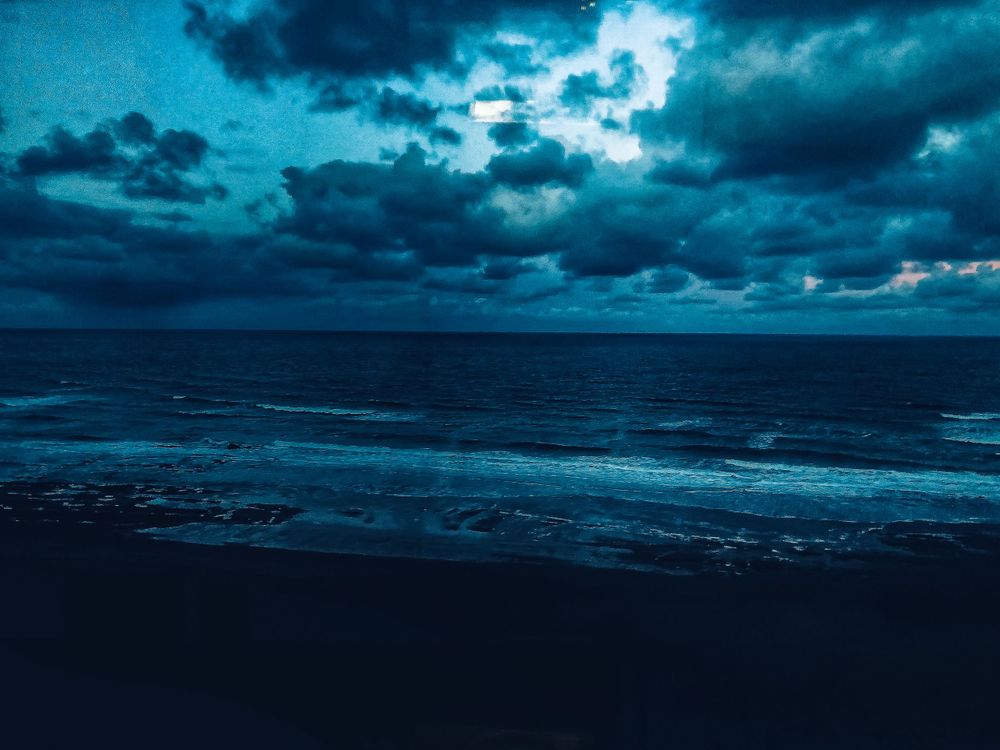 Moody seascape with dark turquoise waves under stormy clouds at twilight.