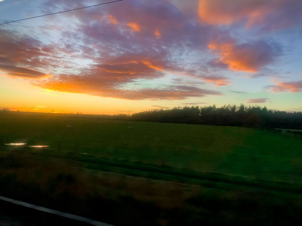 Dramatic sunset over rolling green hills with golden light filtering through colorful clouds.