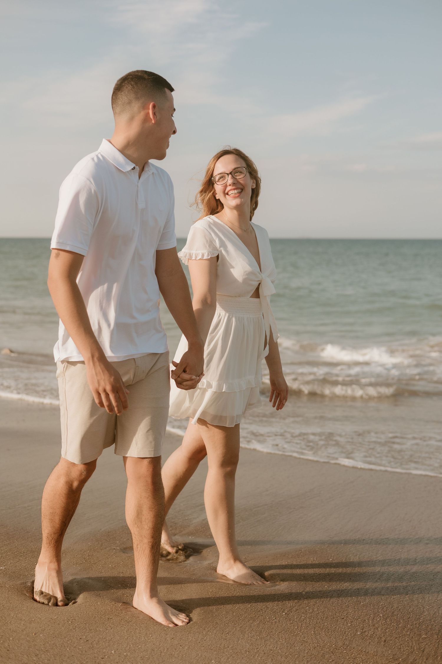 Couples walking barefoot together on sandy beach at sunset.