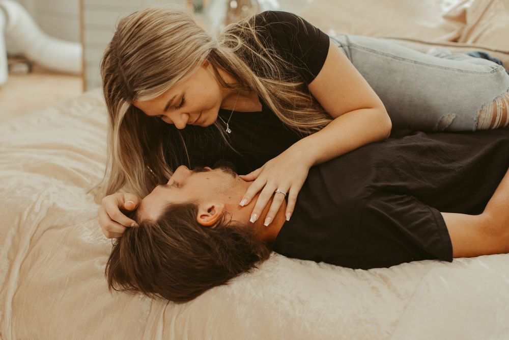 Romantic couple embraces while lying on hardwood floor during cozy indoor photoshoot.