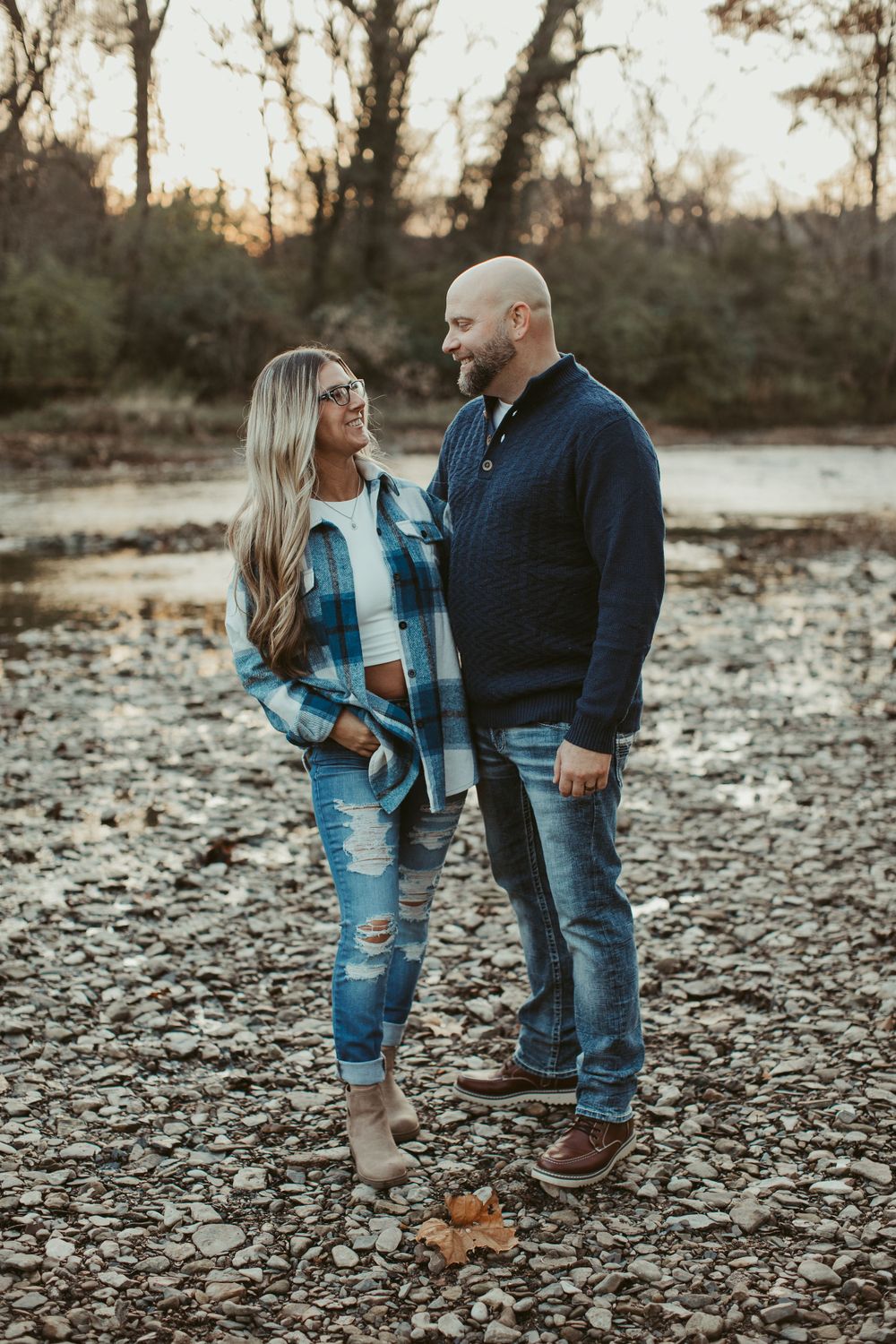 A couple stands together on rocky terrain during a sunset photoshoot.