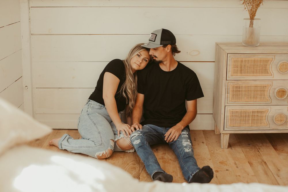 Couple in casual attire poses together during indoor portrait session with natural lighting.