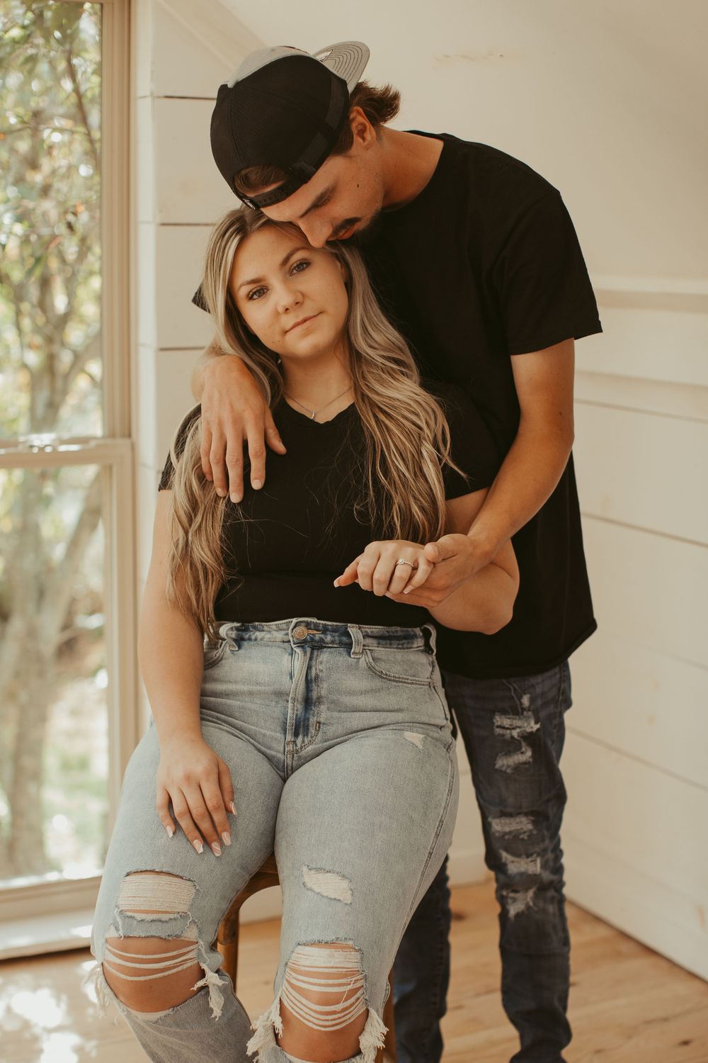 Couple wearing black and denim poses intimately against white wall during photoshoot.