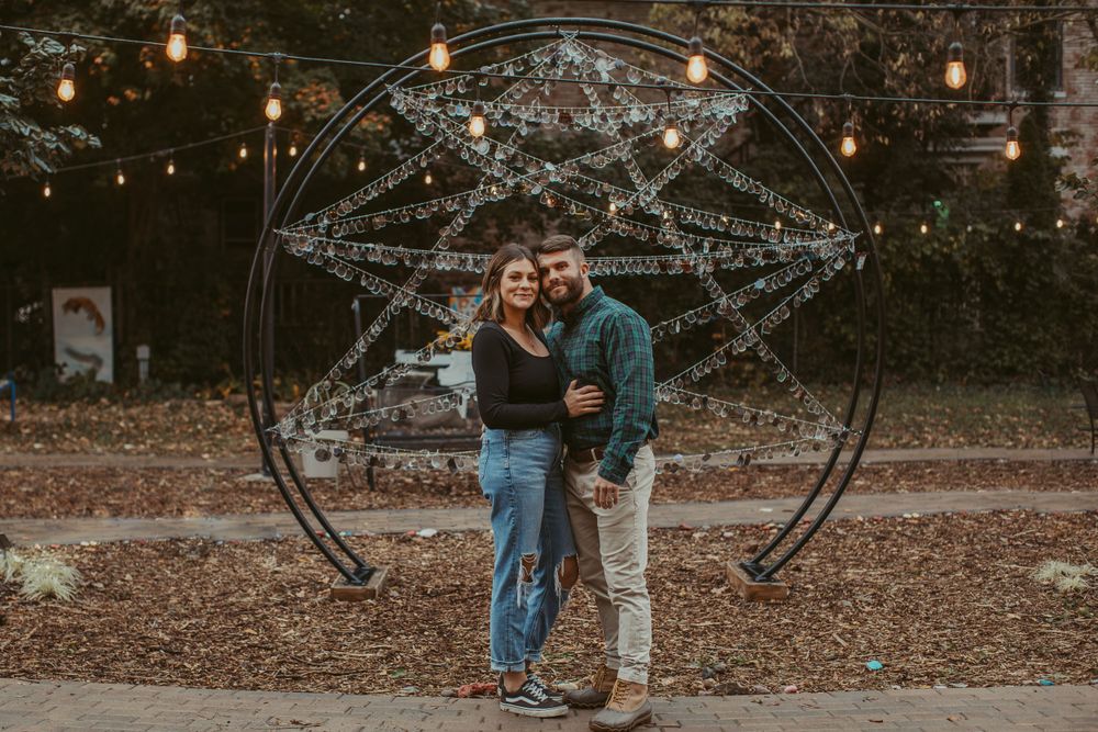 A couple poses under an arch decorated with string lights and crystal garlands.