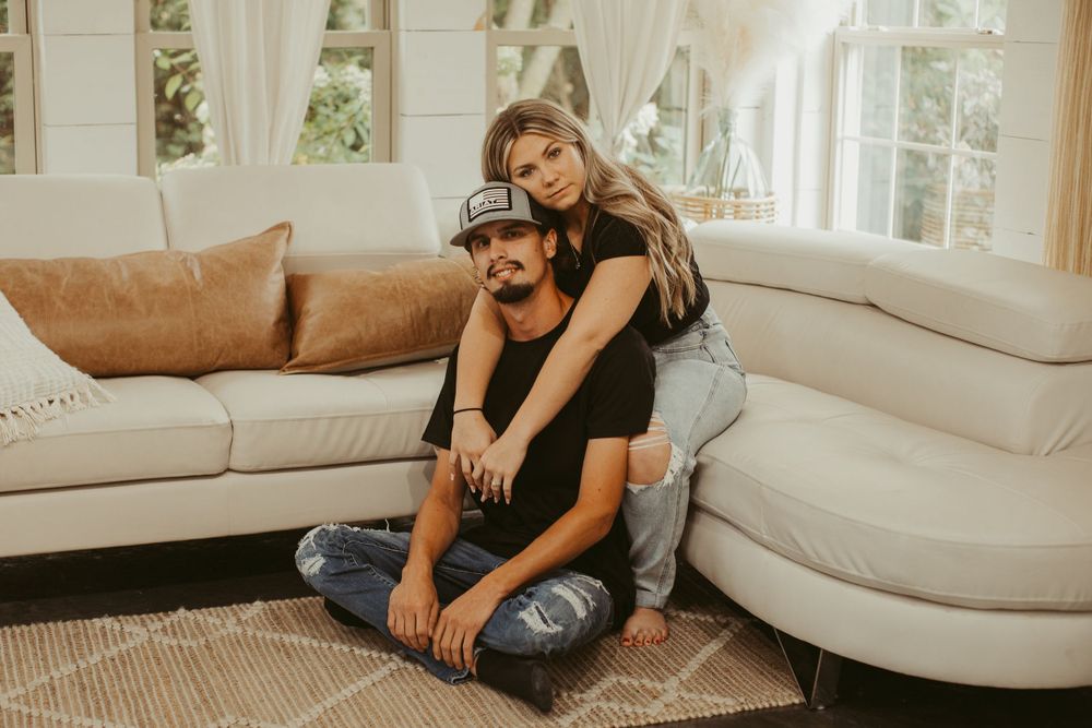 Couple lounges intimately on white sofa during indoor lifestyle photography session.