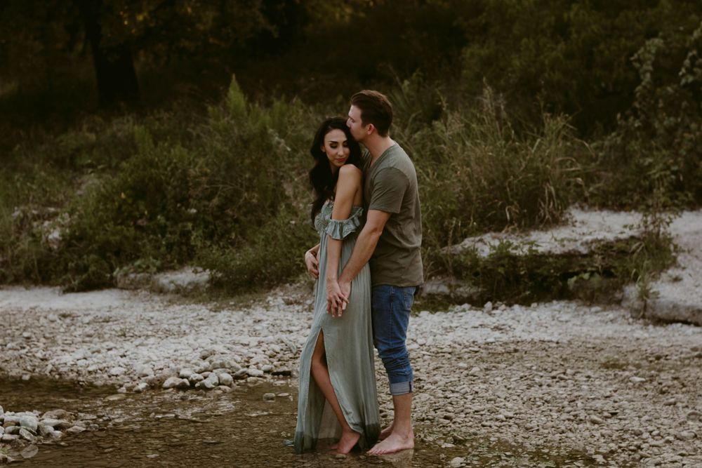 Couple sharing an intimate moment while standing on rocky terrain near water.