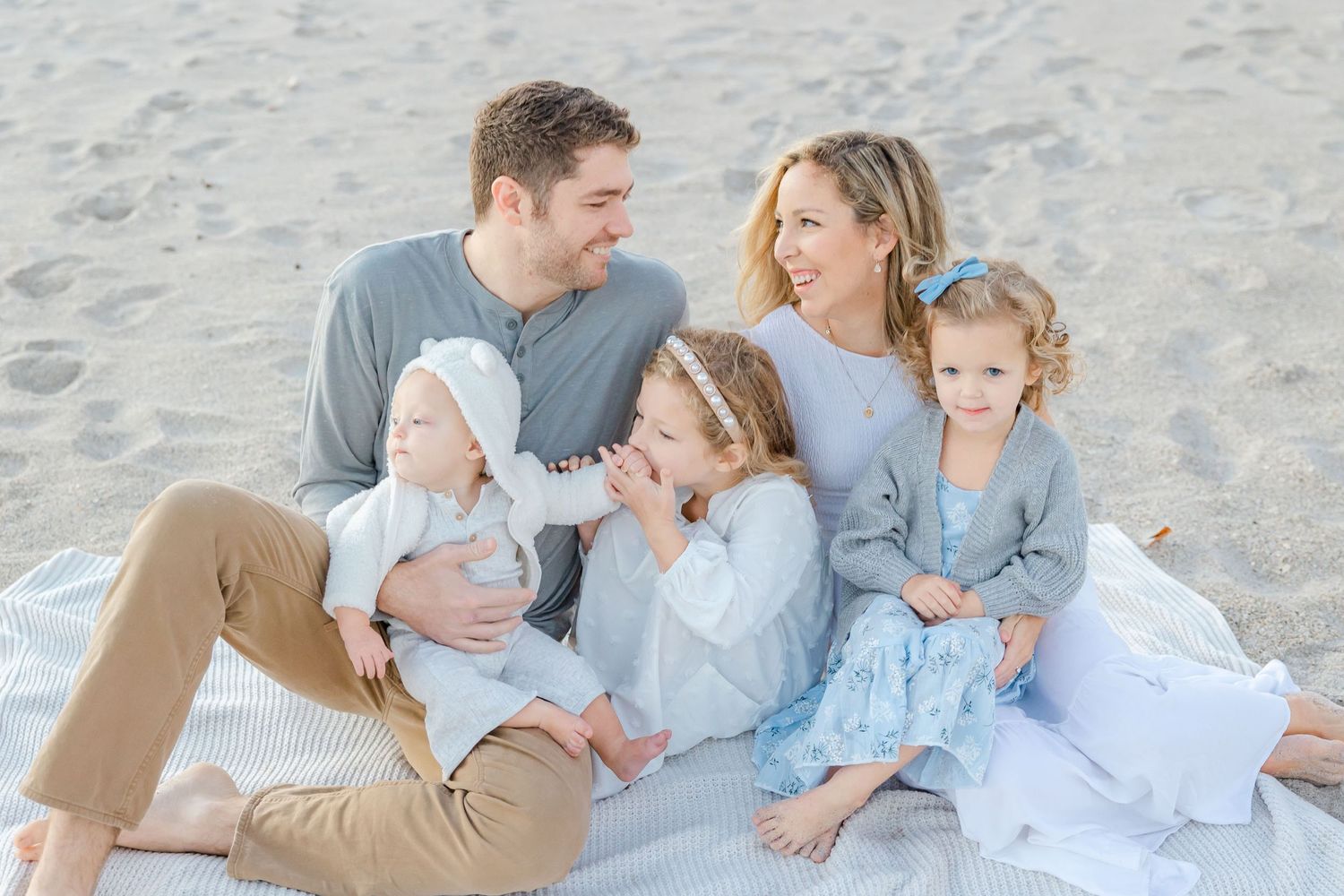 mom and dad looking at each other with 3 kids in their lap on the beach, Space Coast FL Photographer