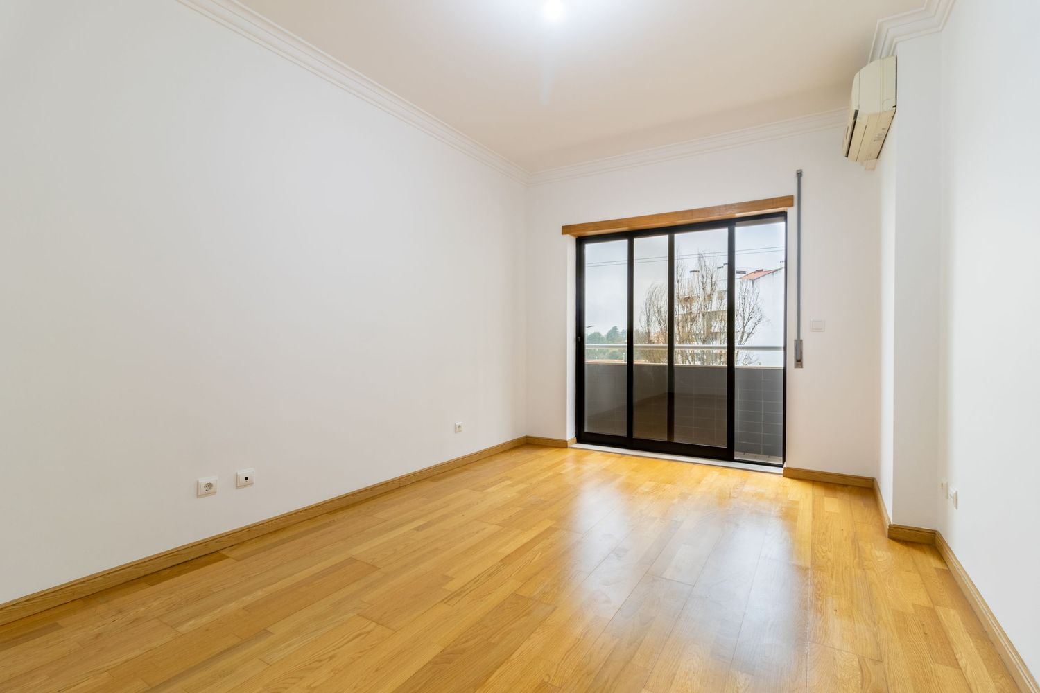 Empty apartment interior with hardwood flooring and large windows letting in natural light.