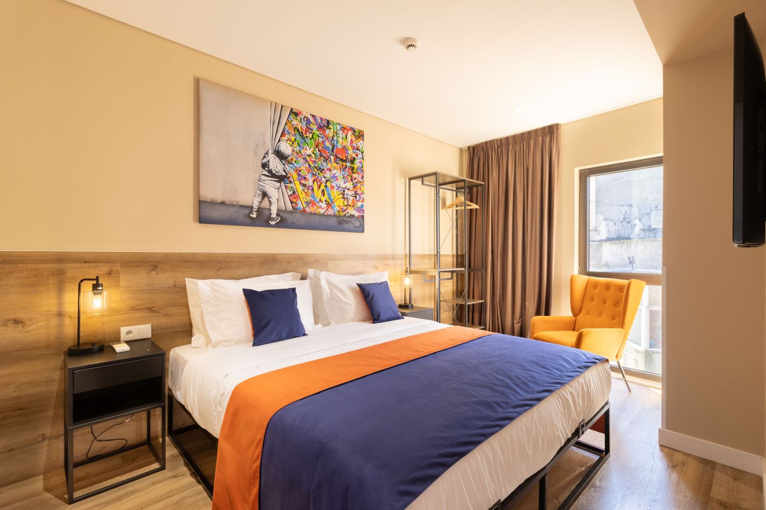 Modern bedroom with blue bedding, orange accents, and wooden headboard wall panel.