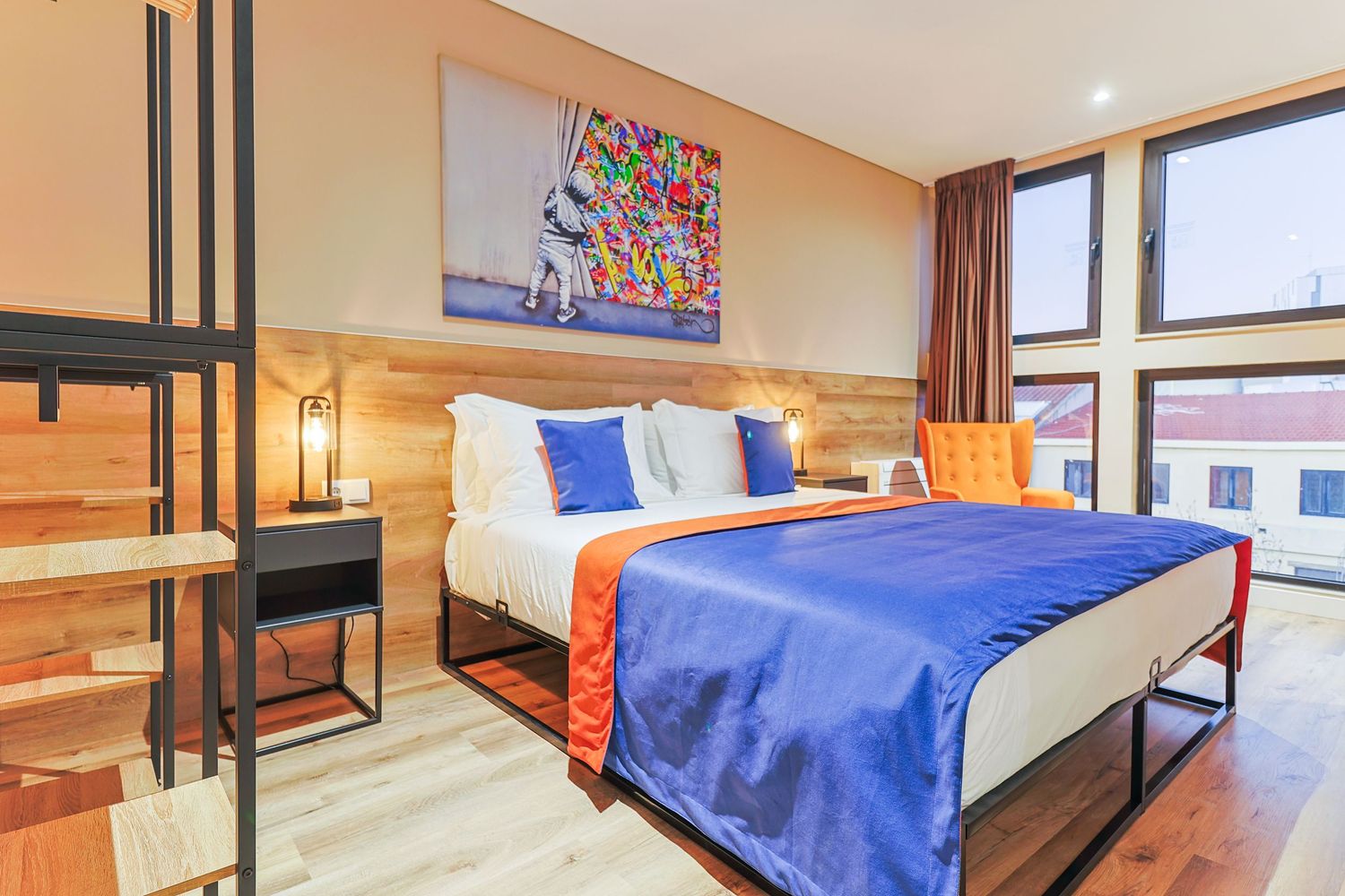 Contemporary hotel room with blue and orange decor featuring large windows and wooden accents.