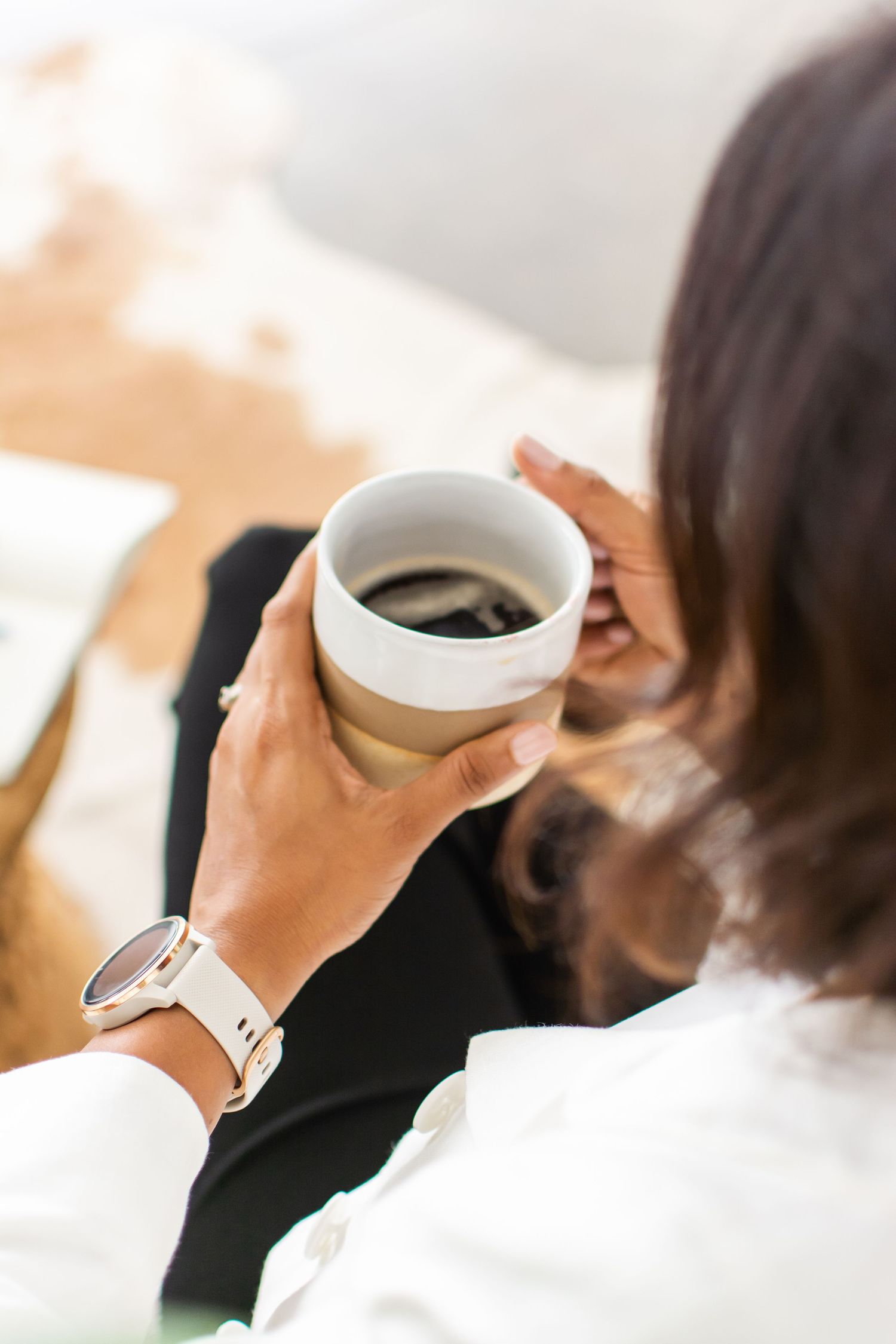 Close-up view of hands holding white ceramic coffee cup with warm lighting.